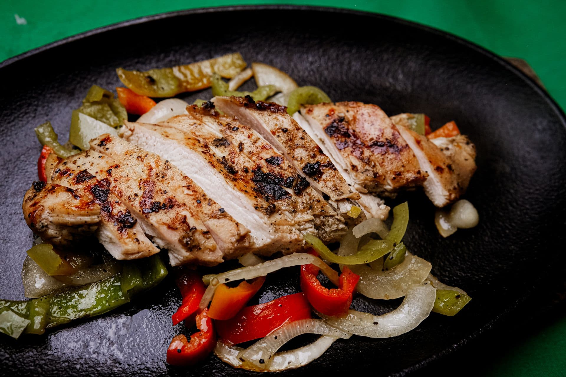 Sliced grilled chicken breast with charred edges over sauteed bell peppers and onions on a cast-iron plate