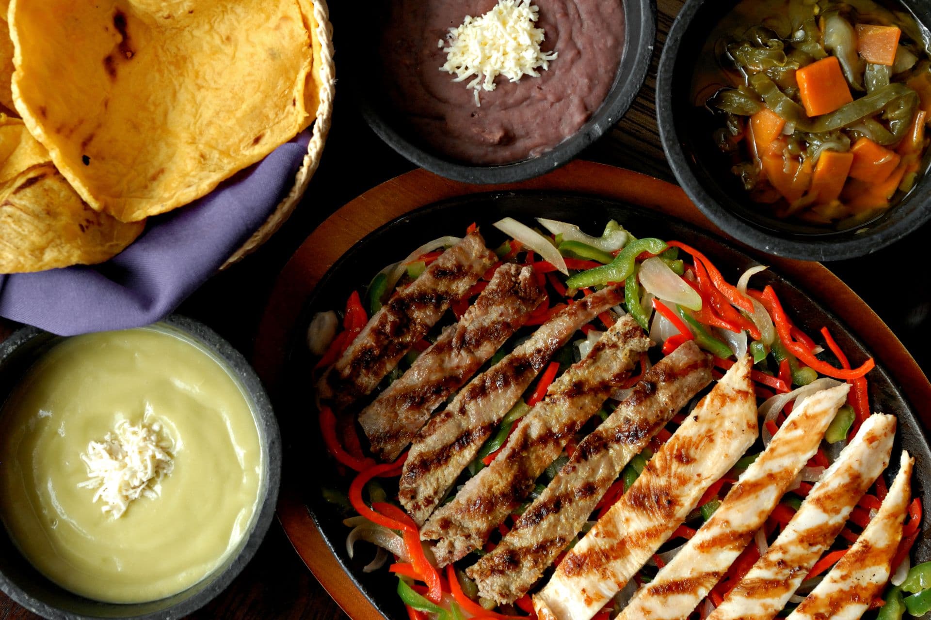 Overhead fajita platter with grilled steak and chicken, peppers, tortillas and sauces