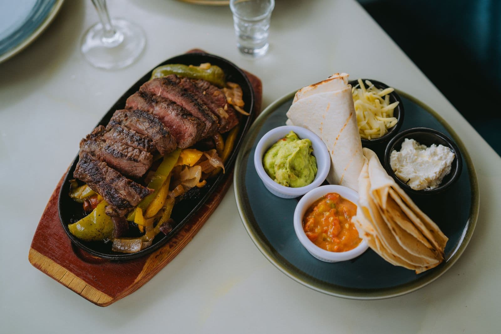 Sliced grilled steak with peppers and onions in a cast-iron skillet with tortillas and salsa