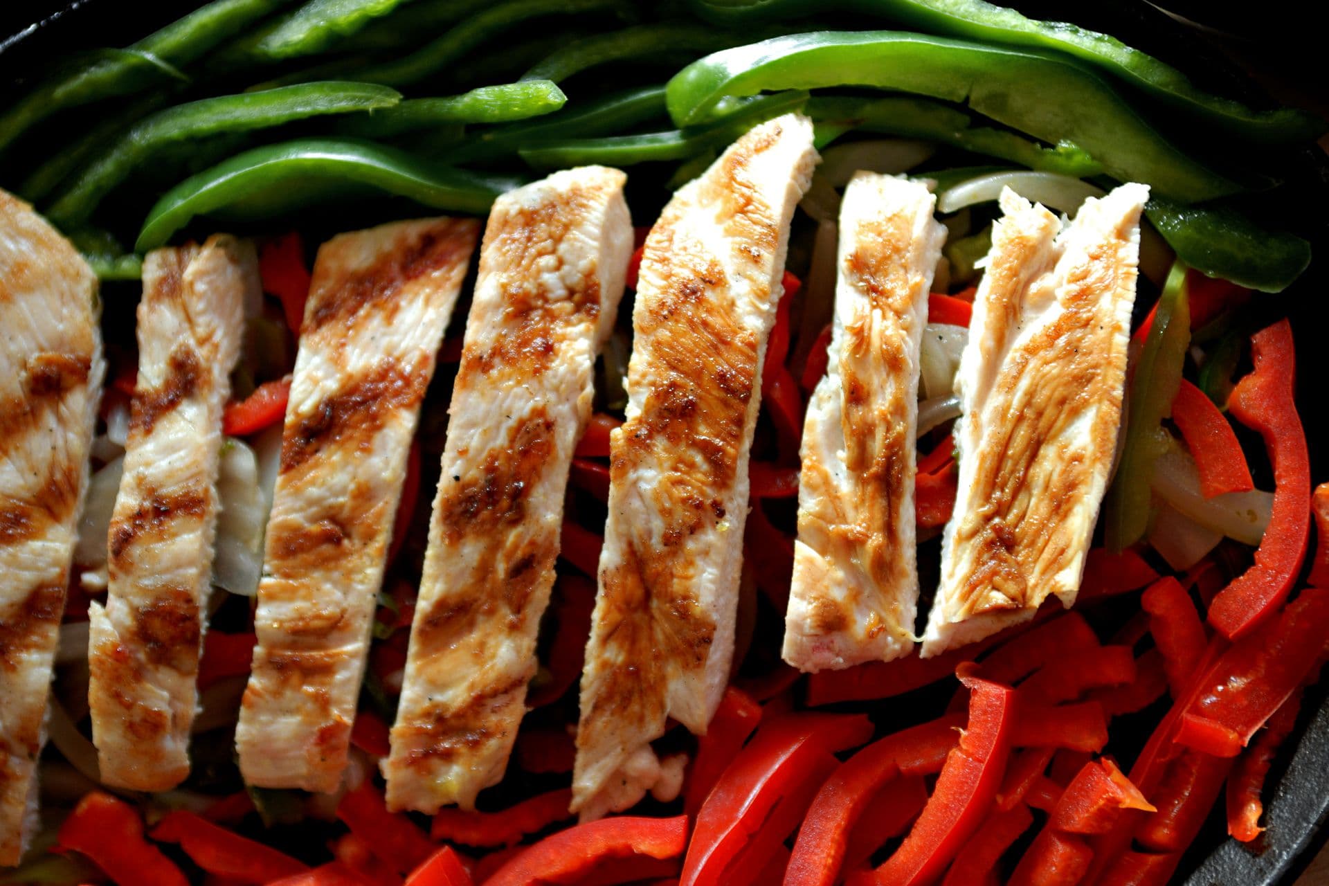Close-up of grilled chicken fajita strips with grill marks over red and green bell peppers