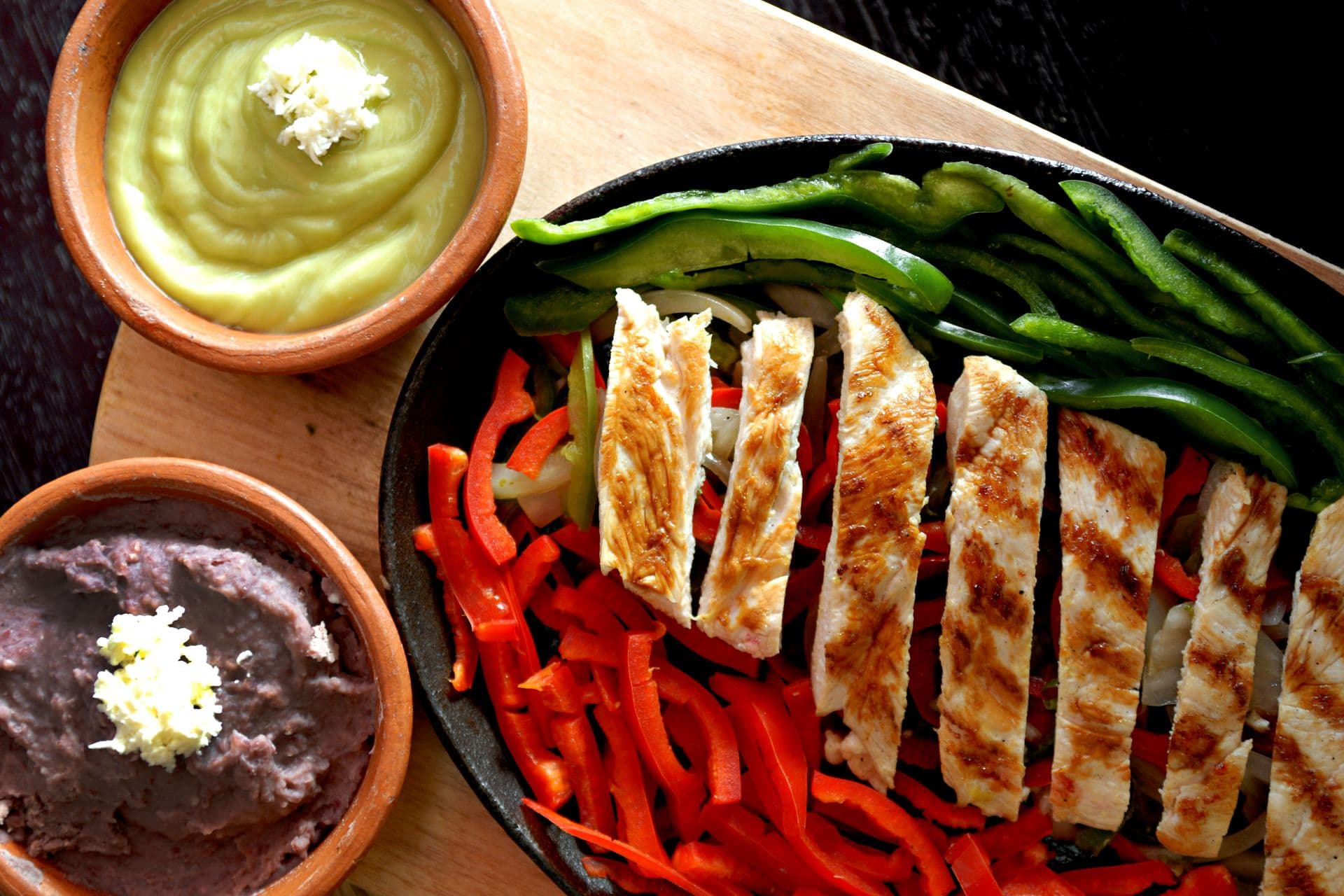 Overhead of grilled chicken fajita strips with peppers, avocado crema and refried beans