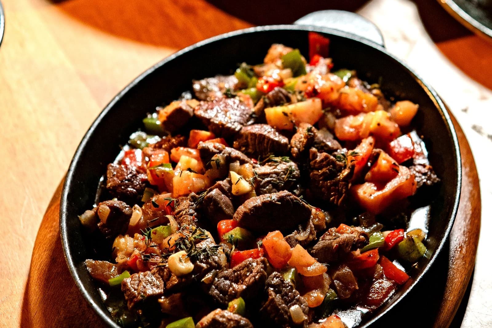 Seared steak pieces with diced peppers, onions and tomato in a cast-iron dish