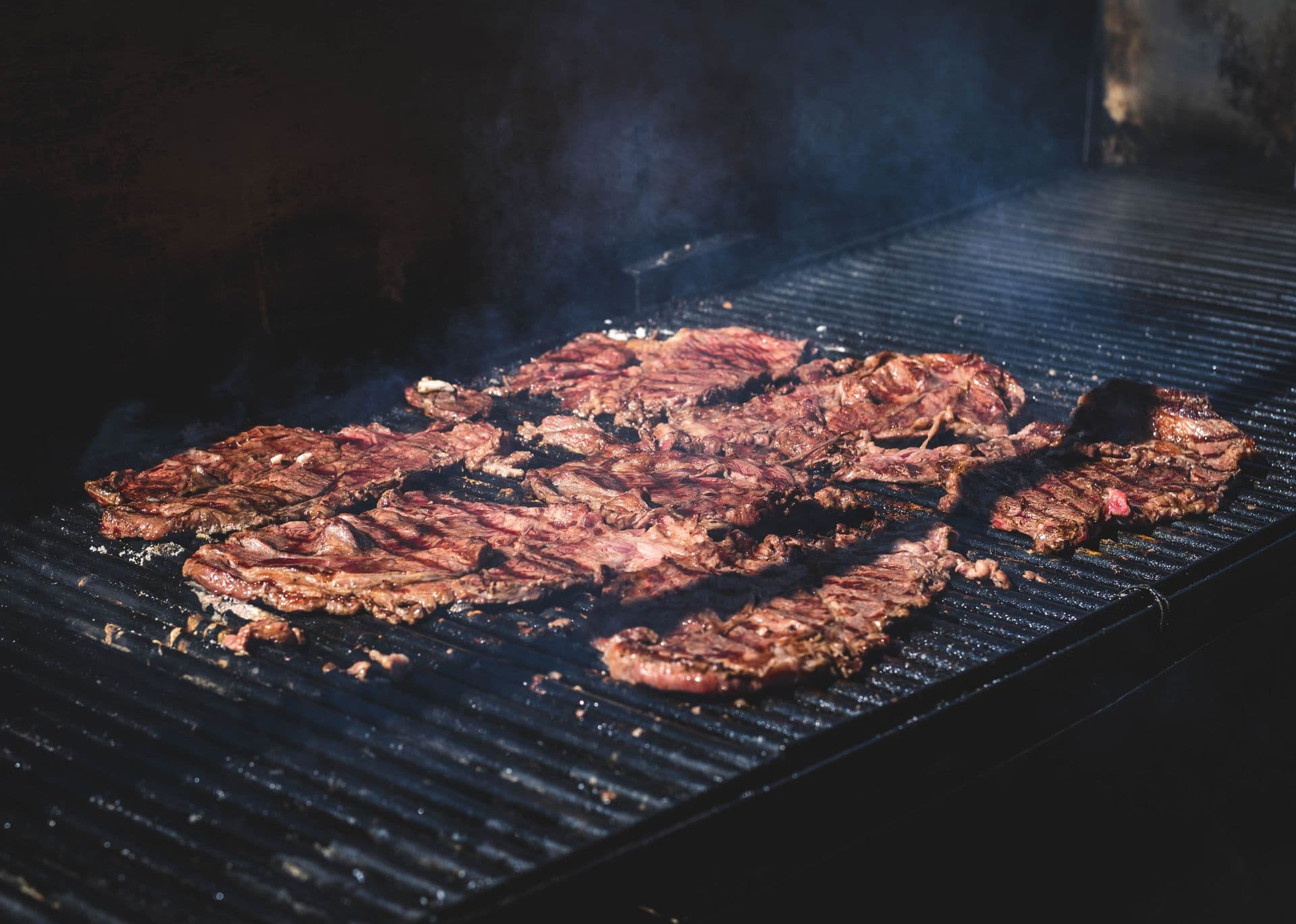 Skirt steak grilling over open flame with rising smoke