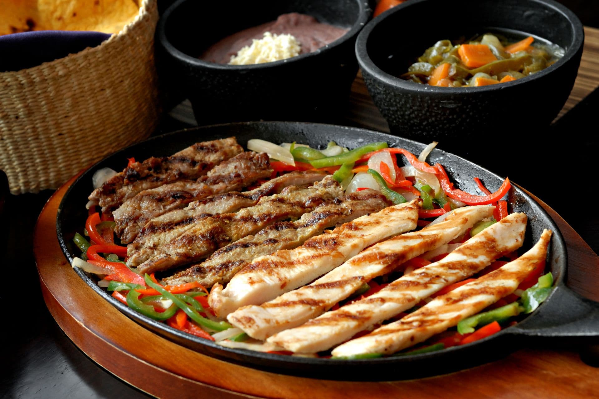 Sizzling steak and chicken fajitas with peppers and onions in a cast-iron skillet